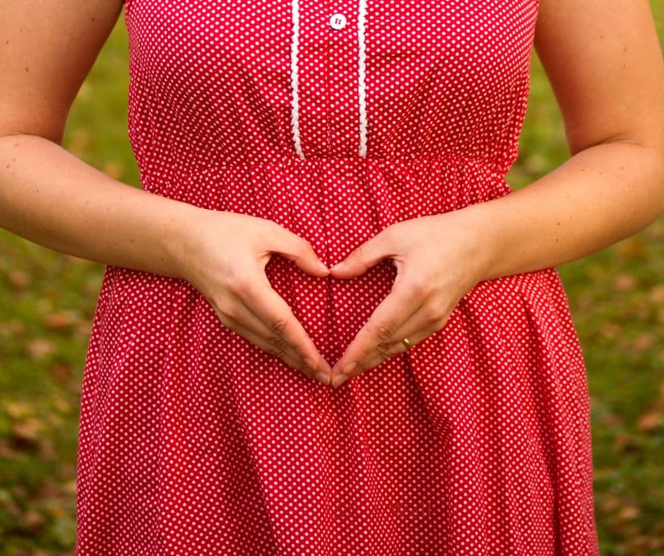 A woman resting her hands over her stomach, fingers forming a heart shape.