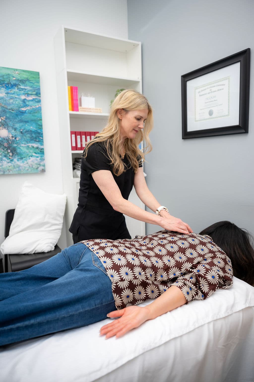 Darcie treating a patient, with her NCCAOM certification visible on the wall.