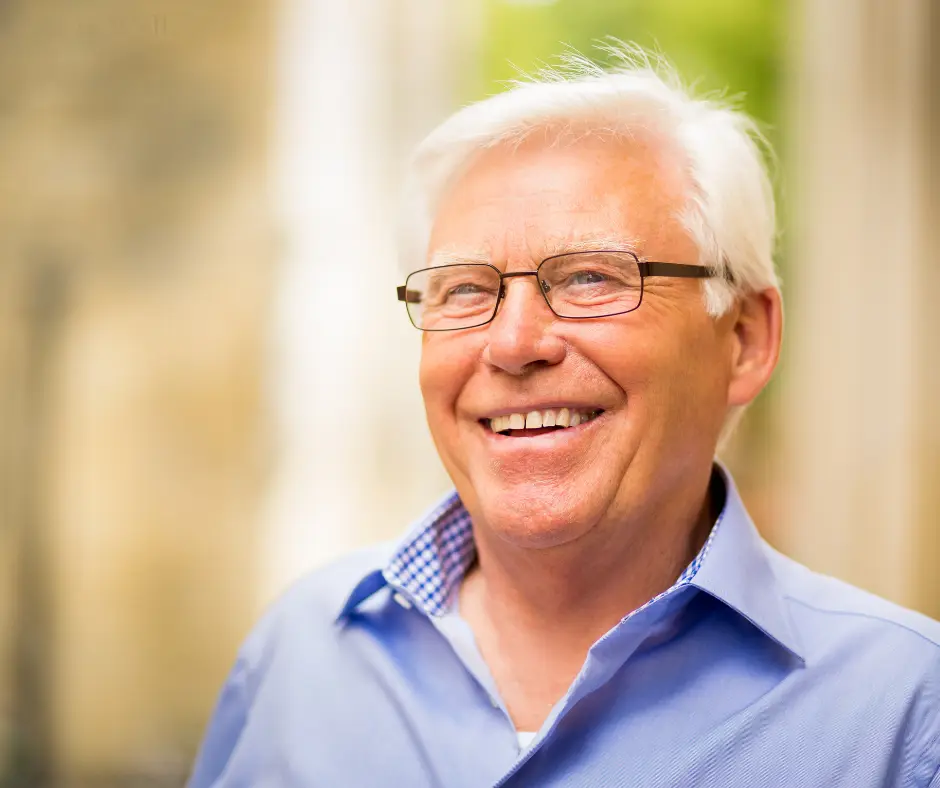 An older man in glasses smiling warmly outdoors.